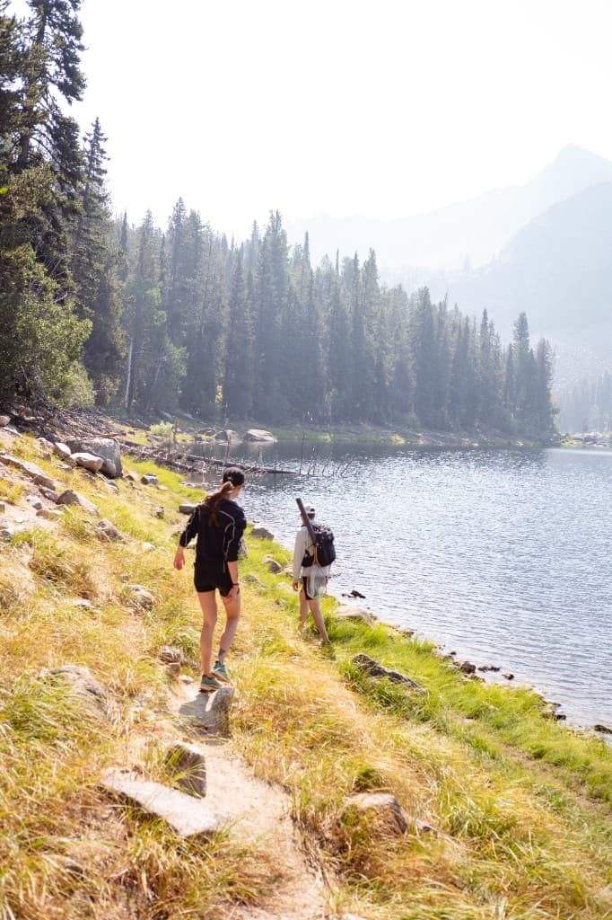 Two hikers on a lakeside trail in Montana with forest and mountains in the background